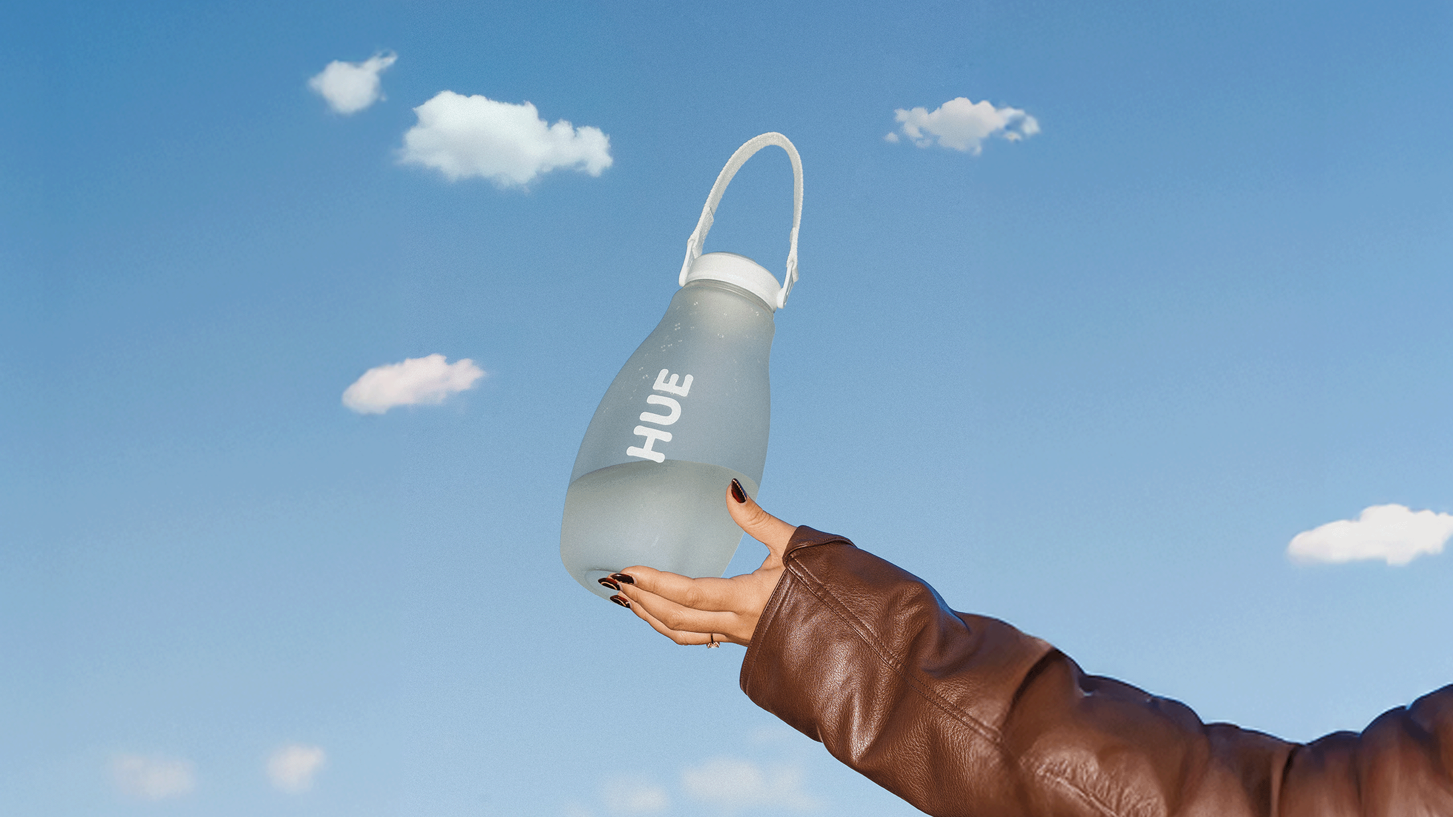 Hand holding a white bottle labeled 'HUE' against a blue sky with white clouds