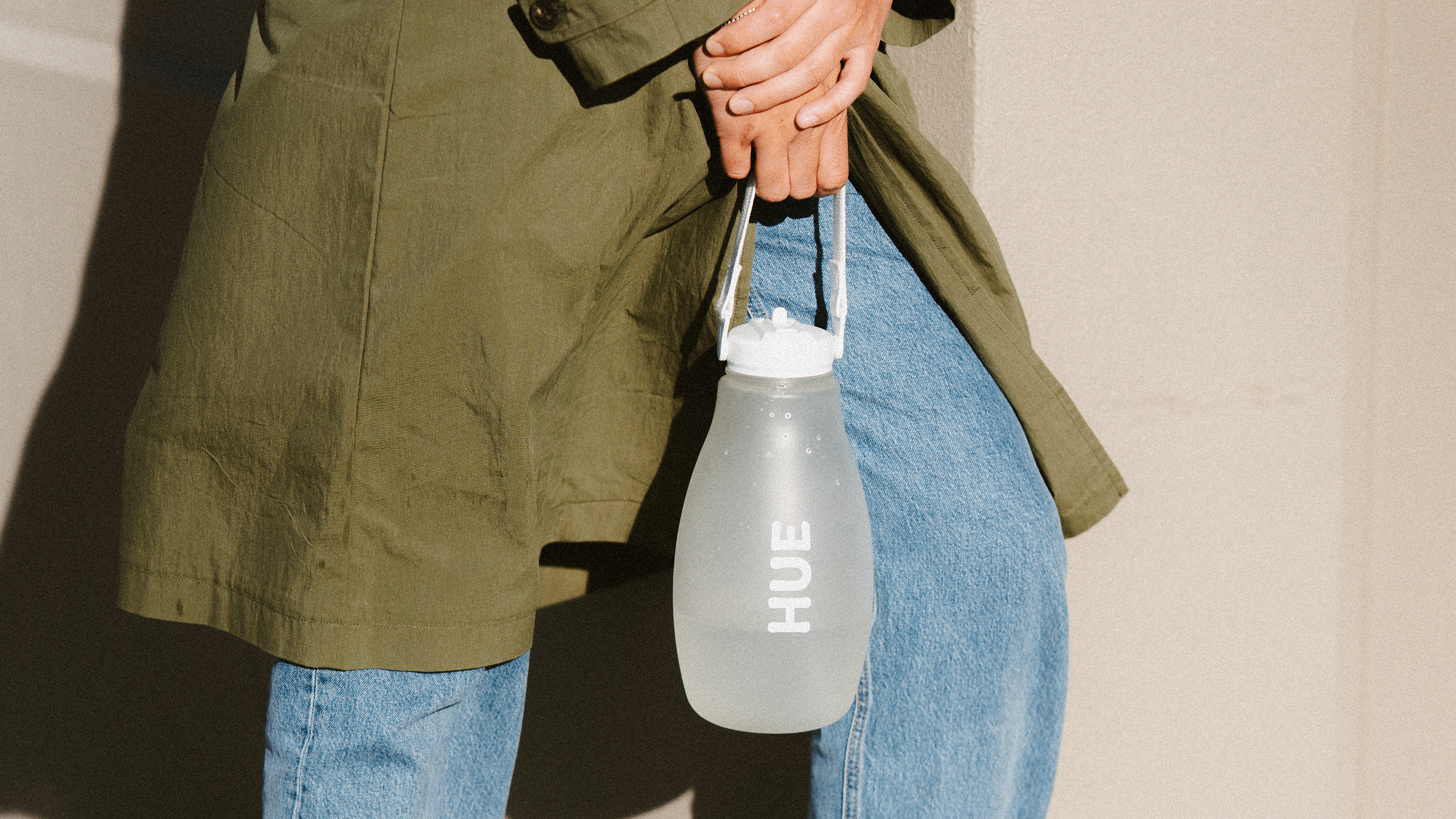 Person holding a clear water bottle with 'HUE' branding against a neutral background